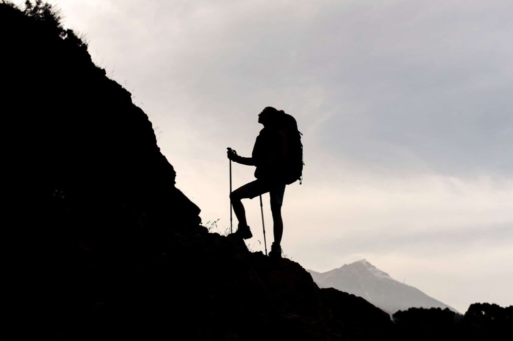 Woman standing rocks with hiking backpack walking sticks